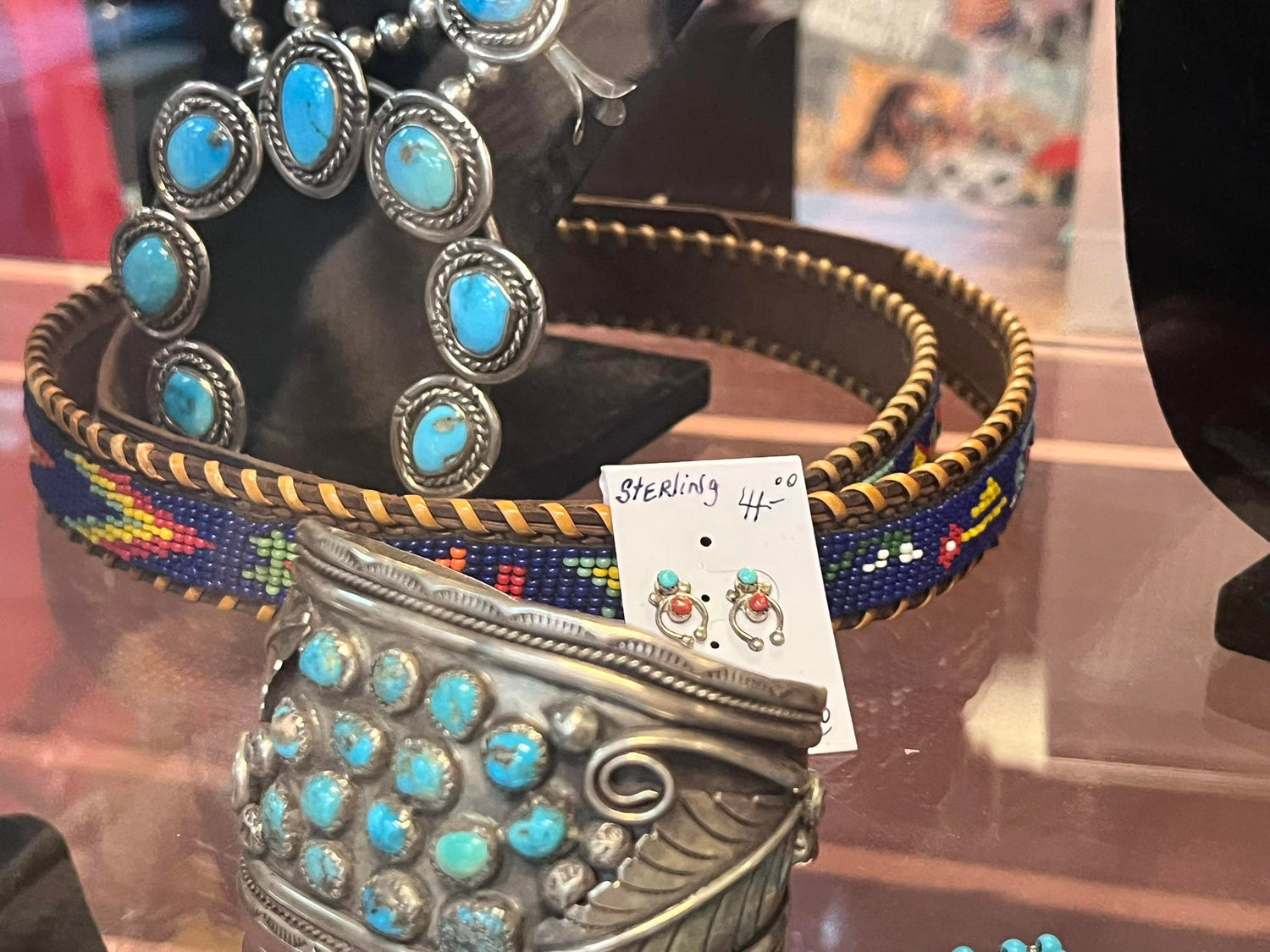 Display of rocks and minerals on tiered wooden stands inside a glass case, featuring amethyst clusters, rose quartz, geodes, fossils, and crystal specimens, some mounted on decorative stands, with handwritten information cards visible.